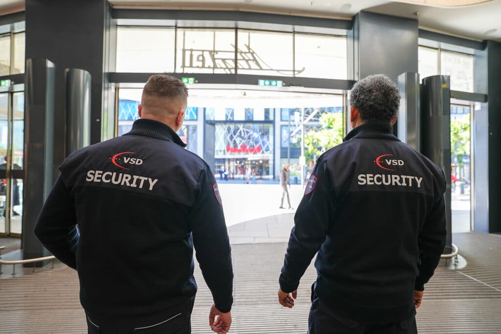 VSD Victory Sicherheitsdienste GmbH – zwei Security-Mitarbeiter beim Eingangsschutz eines Einzelhandelsgebäudes in der Frankfurter Zeil mit Blick auf die Einkaufsstraße